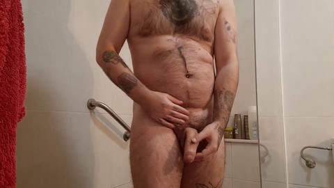Un homme musclé avec un corps poilu urine avant la douche et se fait plaisir jusqu'à atteindre l'orgasme
