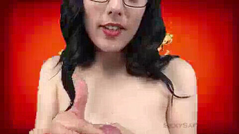 Saffron Bacchus gives a public blowjob on a green screen set while wearing glasses and lipstick