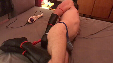 Bound submissive slave gagged with a fuck-stick fights against restraints in a hog-tie