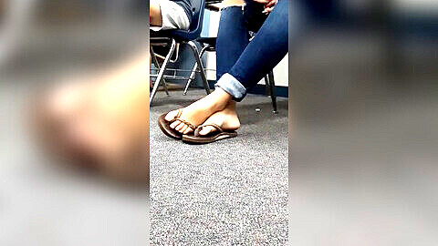La chica juguetona mueve los dedos de los pies y balancea sus sandalias en clase.