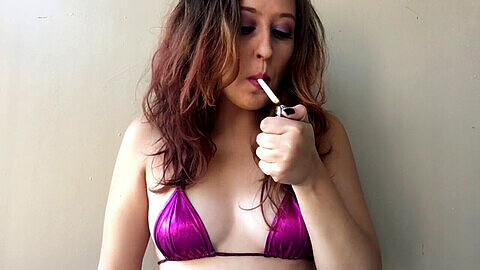 Babe brune fume une cigarette en haut de bikini rose avec seins mignons.