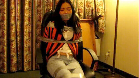 Bella ragazza asiatica legata a una sedia e imbavagliata con nastro adesivo in una sessione di bondage hardcore!
